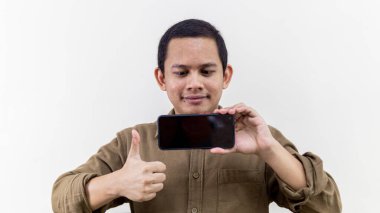 Asyalı genç Malezyalı 'nın gülümseyen yüz ifadesi başparmaklarını kaldırıyor ve boş siyah ekranlı akıllı telefonu izole beyaz arka planda tutuyor..