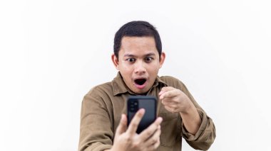 Asyalı genç Malezyalı adamın izole edilmiş beyaz arka plandaki akıllı telefon ekranına bakıp işaret ettiği şok olmuş yüz ifadesi..