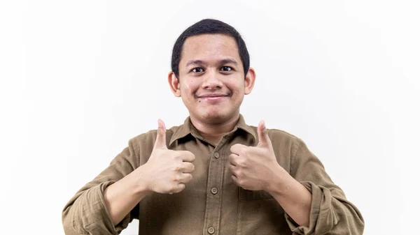令人印象深刻的年轻的亚裔马来人的脸反应 他的两个大拇指向上 棕色衬衫的背景是孤立的白色背景 — 图库照片