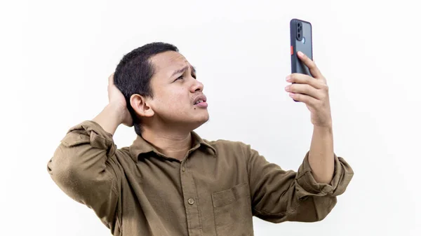 年轻的亚裔马来人苦苦挣扎的面部表情 在孤立的白色背景下寻找智能手机的覆盖 男人强调要建立互联网和电话线网络 — 图库照片#