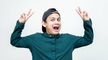 Yakışıklı, çekici, neşeli Asyalı, şapkalı, V işareti ya da barış gösteren, izole edilmiş beyaz arka planda eğlenen Malezyalı bir adamın portresi..