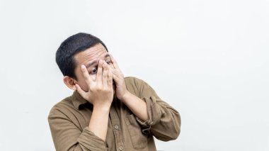 Utangaç Asyalı Malezyalı genç adamın şok olmuş yüz ifadesi, avuç içlerini parmaklarıyla kapatıyor, utanç duyuyor, izole edilmiş beyaz arka planda yüzünü örtüyor..