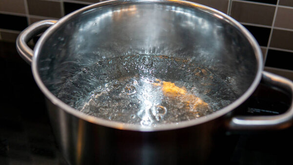 Close up view of hot boiling water in a pot at the kitchen. Water produce bubbles when heated. Selective focused on subject.