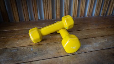 Ahşap arka planda 1 kilogram sarı küçük dambılların yakın görüntüsü. Egzersiz aracı ve fitness ekipmanı.