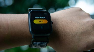 Bileğindeki ip atlama egzersizini kaydetmek için akıllı gözlüklü bir adamın yakın görüntüsü. O, saat şeklinde takılabilir bir bilgisayardır. Verileri akıllı telefona senkronize edebiliyor. Seçici odak.