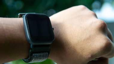 Yakından bakınca bileğinde siyah dokunmatik ekranı olan akıllı bir adam görüyorum. O, saat şeklinde takılabilir bir bilgisayardır. Verileri akıllı telefona senkronize edebiliyor. Nesneye seçici odaklanma.