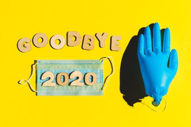 GoODBYE 2020 kelimeleri, sarı arka plandaki ahşap harfler, şişirilmiş tıbbi eldiven ve yüz maskesi. 2020 ve salgın konsepti.