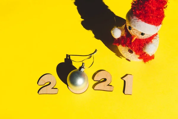 Números de madera 2021, muñeco de nieve y una bola de Navidad de plata sobre un fondo amarillo. —  Fotos de Stock