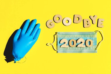 GoODBYE 2020 kelimeleri, sarı arka plandaki ahşap harfler, şişirilmiş tıbbi eldiven ve yüz maskesi. 2020 ve salgın konsepti.