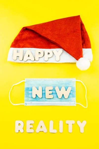 Cappello Babbo Natale, maschera protettiva e lettere in legno HAPPY NEW REALITY su sfondo giallo. — Foto Stock