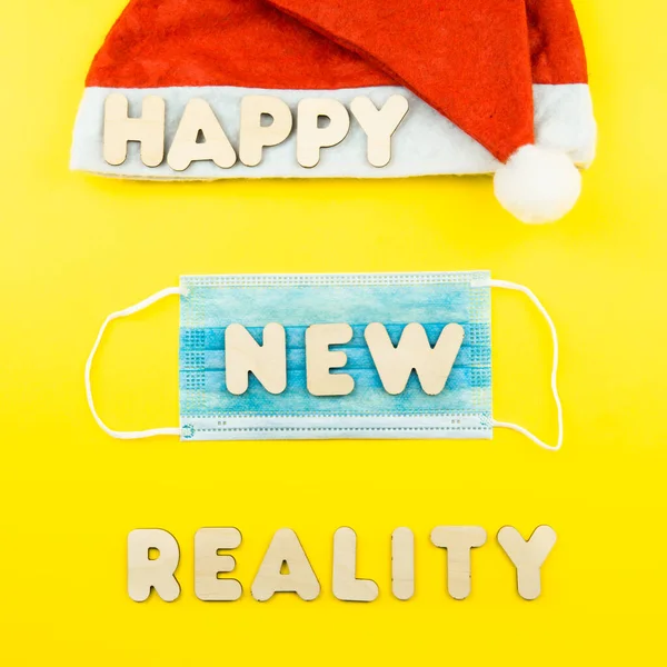 Cappello Babbo Natale, maschera protettiva e lettere in legno HAPPY NEW REALITY su sfondo giallo. — Foto Stock