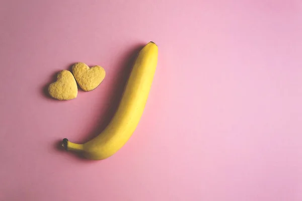 Zwei Kekse in Herzform nebeneinander und Banane auf rosa Hintergrund. Das Konzept des Valentinstags. — Stockfoto