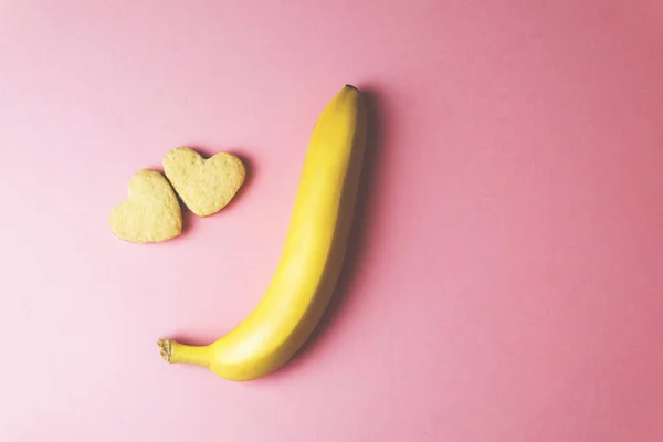 Zwei Kekse in Herzform nebeneinander und Banane auf rosa Hintergrund. Das Konzept des Valentinstags. — Stockfoto