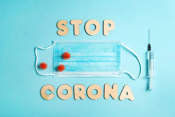 Words STOP CORONA from wooden letters, syringe and facemask. Vaccination and the end of epidemic concept.