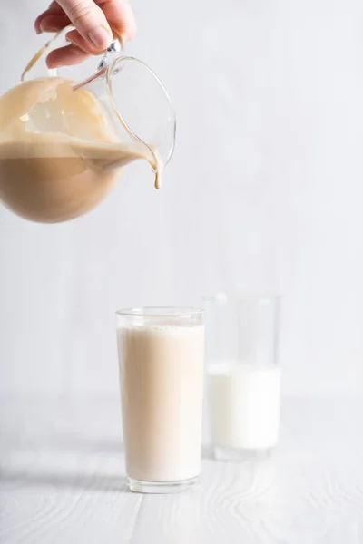 Dalgon brown coffee mixture is poured from the decanter into a glass of milk. Milkshake with instant coffee and sugar, whipped until thick foam. — Photo
