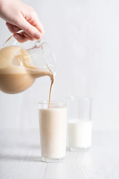 Dalgon brown coffee mixture is poured from the decanter into a glass of milk. Milkshake with instant coffee and sugar, whipped until thick foam. — Photo