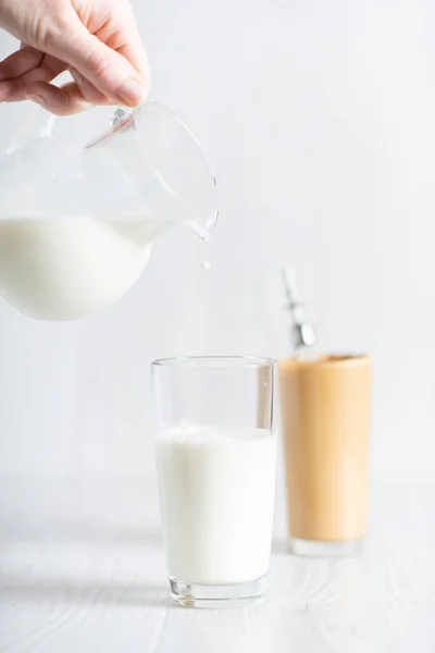 The process of making a fashionable Korean drink dalgonacoffee. Glass and decanter with milk on a light background. — Photo