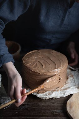İnce keklerden çikolatalı pasta yapmak. Kadın pastayı kremayla süslüyor..