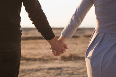 Erkek ve kadın gün batımında kumsalda el ele tutuşuyorlar. Görüntü tonu tahıl etkisi.