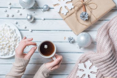 Masanın üzerinde şekerlemeler olan bir fincan kahve. Hediyeler, Noel baloları ve kar tanelerinin yanında..