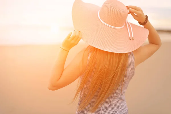 Na plaży, młoda kobieta z blond włosami w różowym kapeluszu spogląda w dal, podnosząc ręce. koncepcja odpoczynku i relaksu — Zdjęcie stockowe