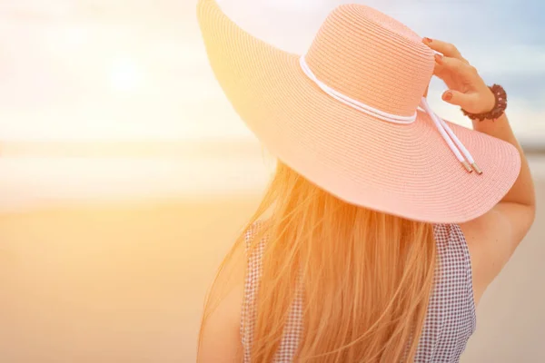 Молодая женщина в шляпе на пляже смотрит на восход солнца над морем. Блестящие светлые волосы. тонизированное изображение и мягкая фокусировка. копировальное пространство — стоковое фото