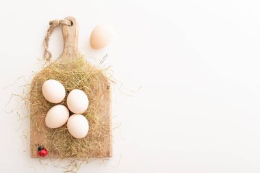 Beyaz yumurtalar kuru çimenlerin ve tahta bir tahtanın üzerinde yatar. Paskalya hazırlığı konsepti. Boşluğu kopyala.