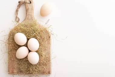 Beyaz yumurtalar kuru çimenlerin ve tahta bir tahtanın üzerinde yatar. Paskalya hazırlığı konsepti. Boşluğu kopyala.