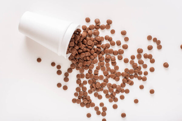 Home confectioner business concept. DIY homemade sweets. Chocolate callets scattered from a disposable cup on a white background. top view close-up. Flat lay.