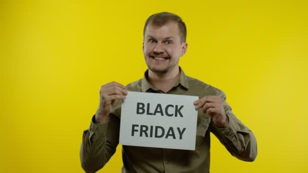 Mężczyzna uśmiecha się i pokazuje napis Czarny Piątek, radujące rabaty, zakupy online — Wideo stockowe