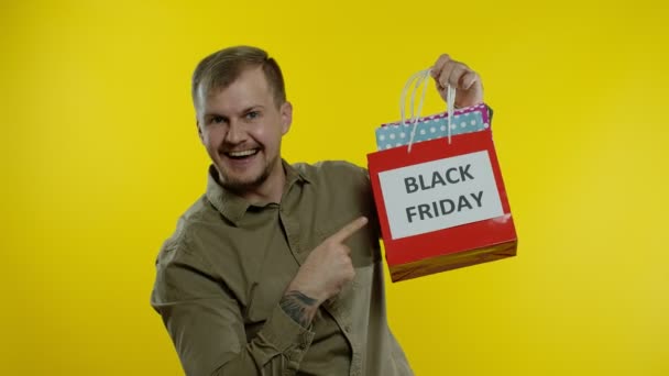 Man toont Black Friday inscriptie op boodschappentassen, glimlachend, tevreden met lage prijzen aankopen — Stockvideo