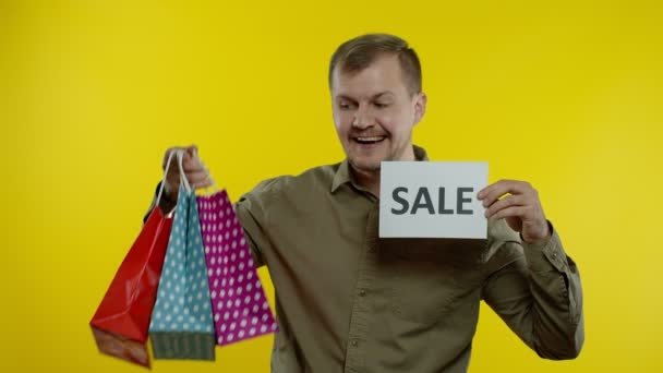 Gelukkig lachende man met boodschappentassen met zwarte vrijdag inscriptie op tassen en Sale word note — Stockvideo