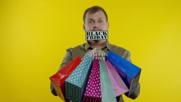 Un bărbat surprins care arată saci de cumpărături și inscripție Black Friday în gură. Fundal galben — Videoclip de stoc