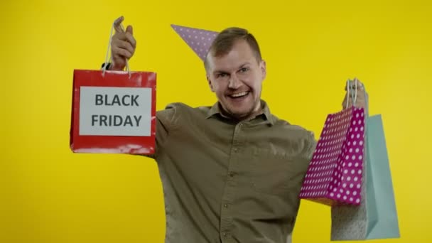 Sonriente hombre mostrando la inscripción Viernes Negro en las bolsas de la compra, celebrando, regocijando buenos descuentos — Vídeos de Stock