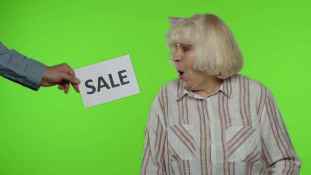 Inscriptie reclame Sale word verschijnt naast vrolijke oma met boodschappentassen. Chromatoetsen — Stockvideo