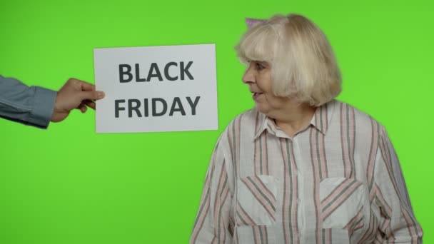 Επιγραφή διαφήμιση Black Friday εμφανίζεται δίπλα στην χαρούμενη γιαγιά με τσάντες ψώνια — Αρχείο Βίντεο