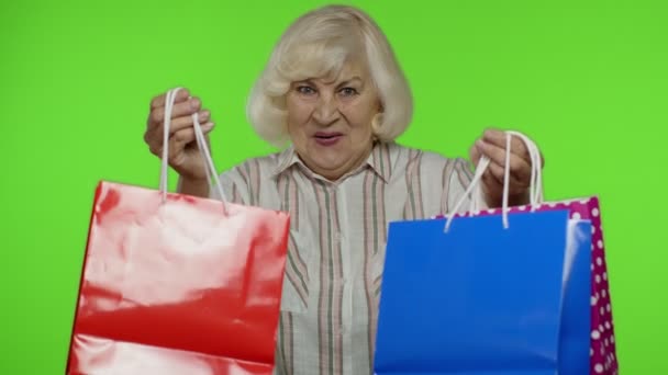 Ηλικιωμένη γιαγιά με πουκάμισο δείχνει Black Παρασκευή επιγραφή σε τσάντες για ψώνια, χαρά εκπτώσεις — Αρχείο Βίντεο