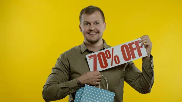 Hombre mostrando hasta 70 por ciento Off inscripción y bolsa de compras, buscando satisfecho con los precios bajos — Foto de Stock