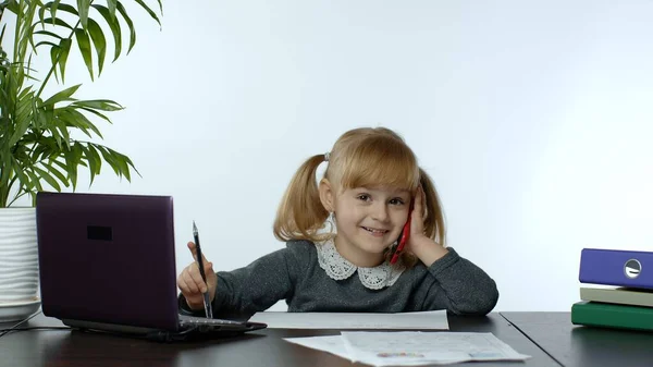 Забавная маленькая девочка-босс менеджер эмоционально разговаривает по мобильному телефону, сидит за компьютерным столом — стоковое фото