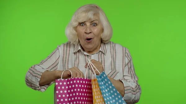 Starsza babcia podnosi torby na zakupy, świętuje, zadowolona z zakupu, rabatu. Klucz chromowy — Zdjęcie stockowe