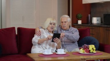 Büyük anne ve büyük baba evde dijital tablet bilgisayar kullanarak konuşup duruyorlar. Coronavirus kilitlenmesi