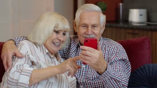 Babcia i dziadek rozmawiają przez internet przez telefon komórkowy w domu. Uśmiechnięta para starców — Wideo stockowe