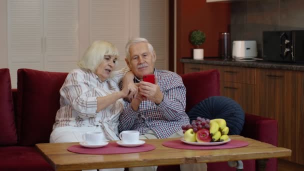 Ancianos abuelos pareja de ancianos hablando y utilizando el teléfono móvil digital en casa. Compras online — Vídeos de Stock