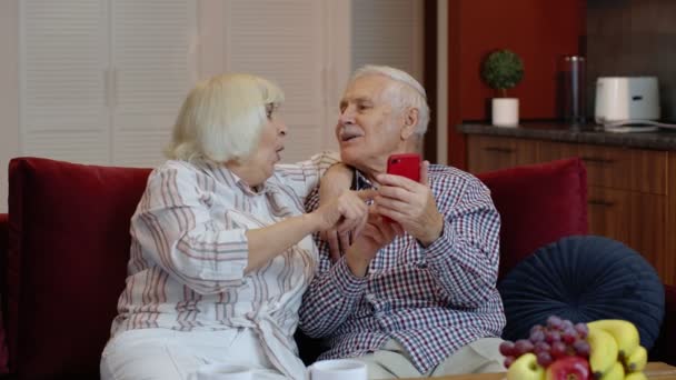 Ancianos abuelos de la vieja pareja hablando y usando la computadora del teléfono móvil en casa. Compras por Internet — Vídeos de Stock