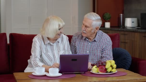 Velhos avós casal sênior falando e usando computador portátil digital em casa. Compras na Internet — Vídeo de Stock