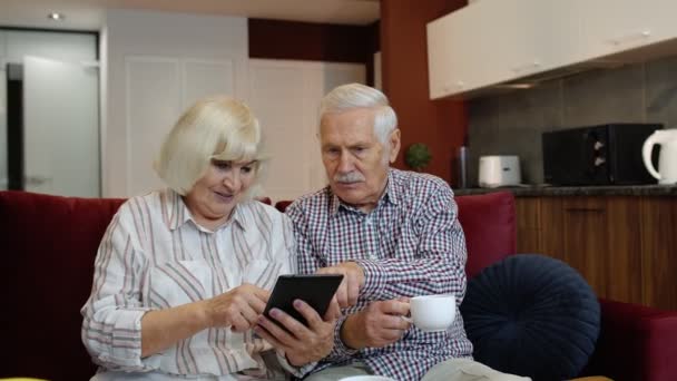 Senior pensionär par med digital surfplatta dator hemma. Vila på soffa i mysigt vardagsrum — Stockvideo