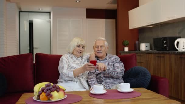 Ancianos abuelos de la vieja pareja hablando y usando la computadora del teléfono móvil en casa. Compras por Internet — Vídeos de Stock