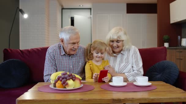 Senior Caucasian couple with cute child girl granddaughter using mobile phone, watching funny videos — Stock Video