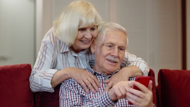 Abuelos mayores pareja hablando y utilizando el teléfono móvil digital en casa. Bloqueo del Coronavirus — Vídeo de stock