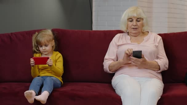 Abuela mayor con nieta niña utilizando el teléfono móvil digital, jugando juegos en casa — Vídeo de stock